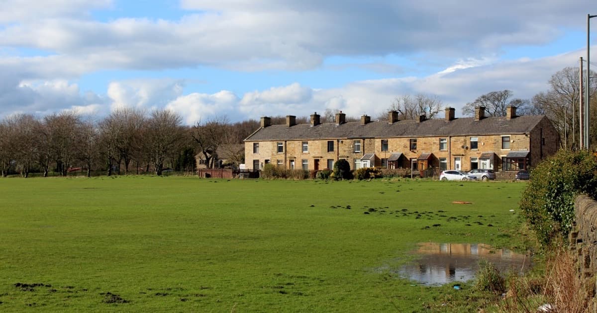 A row of stone terraced houses beside an open green field in Burnley, Lancashire